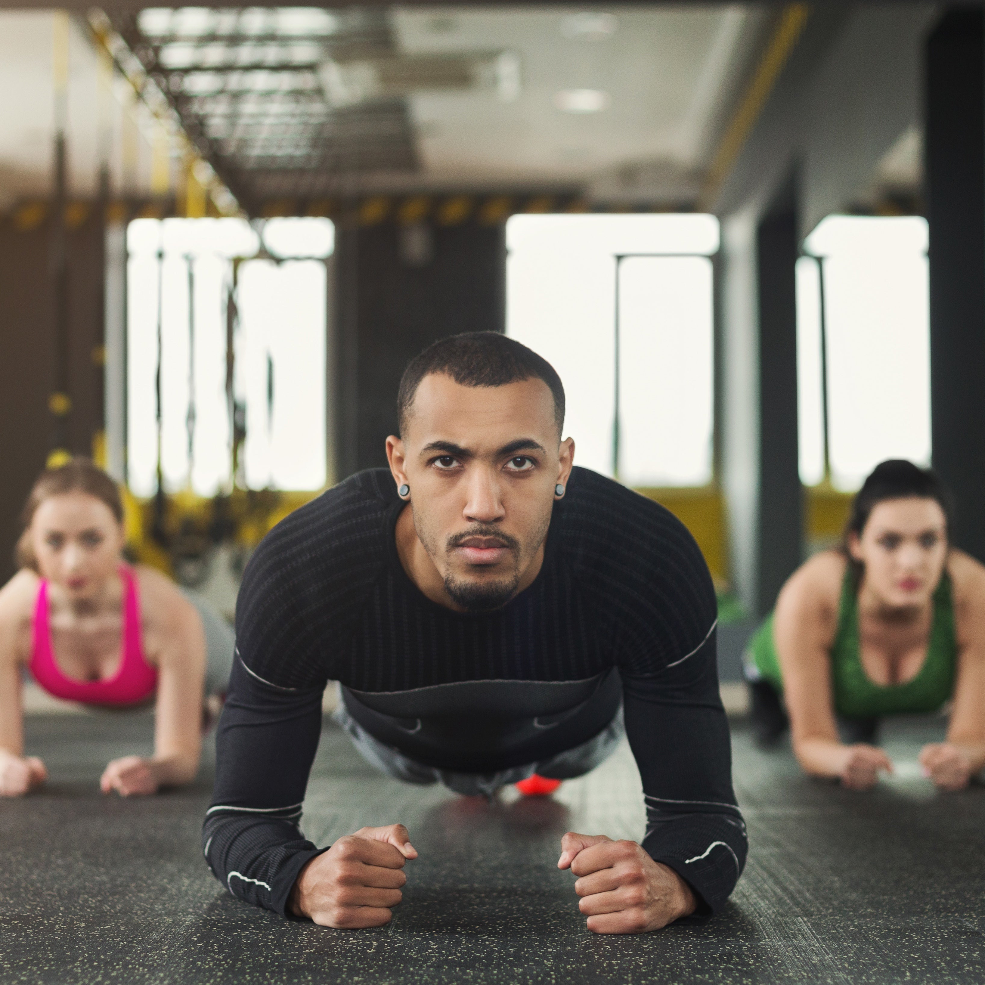 A group of three individuals performing push-ups on dumbbells during an intense workout session, highlighting strength, stability, and group motivation.