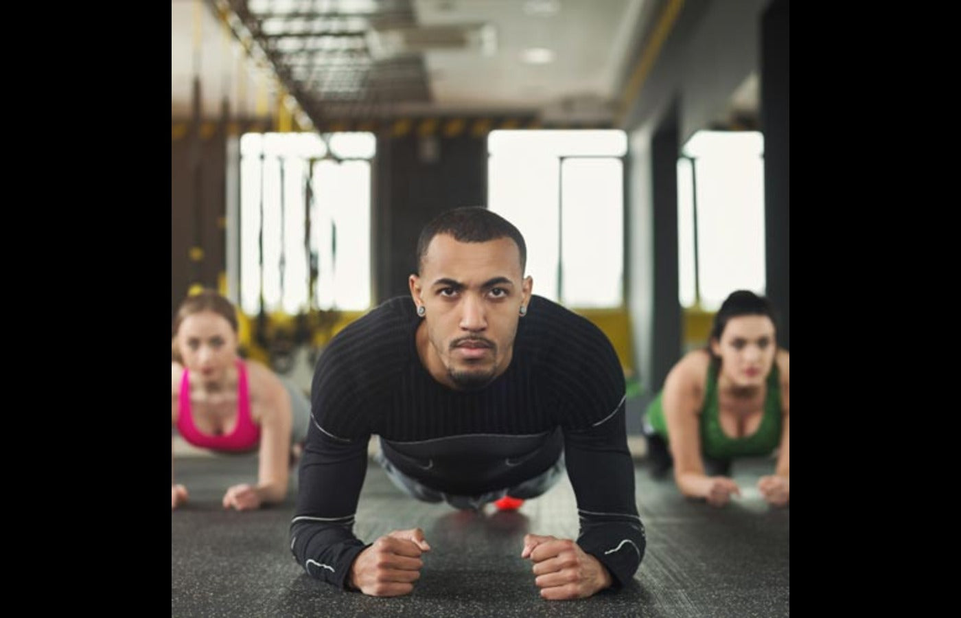 A group of three individuals performing push-ups on dumbbells during an intense workout session, highlighting strength, stability, and group motivation.