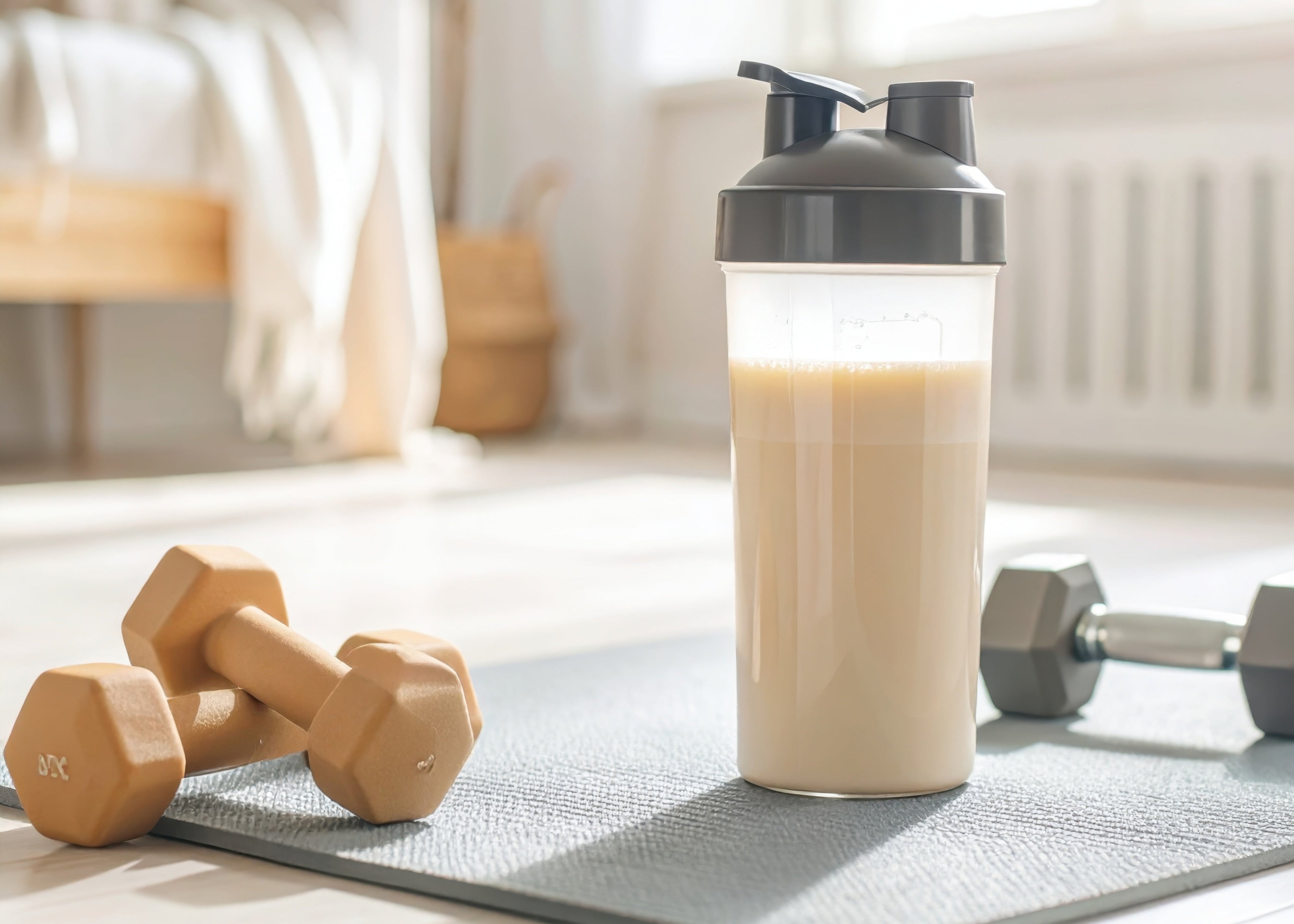 Shaker bottle with a protein shake on a yoga mat with dumbbells and weights in a home setting