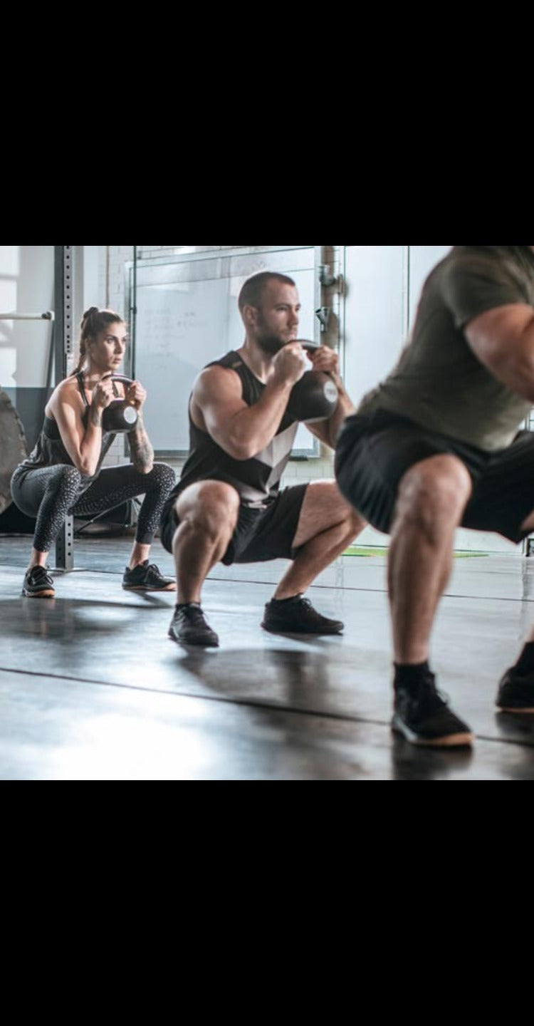 Three people engaged in a group workout, performing squat-to-kettlebell presses in sync, showcasing strength, balance, and teamwork.