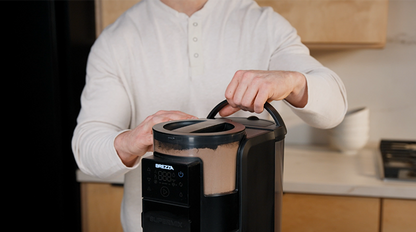 Hands demonstrating how to remove the powder container, water tank, and funnel from the Brezza Supermix for cleaning or refilling